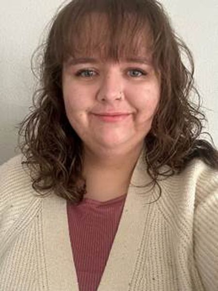 Smiling woman with curly hair wearing a beige cardigan and maroon top — Lily Giesler, LMSW at Flourish Counseling